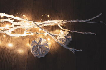 Two white cones near white branches with christmas lights on a wooden background