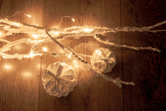 Two white cones near white branches with christmas lights on a wooden background