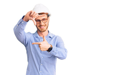 Handsome young man with bear wearing architect hardhat smiling making frame with hands and fingers with happy face. creativity and photography concept.