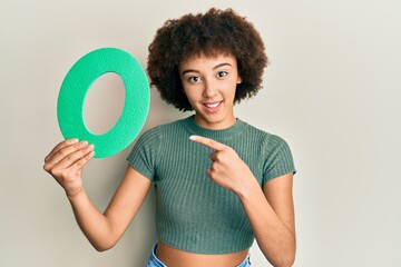 Young hispanic girl holding number zero smiling happy pointing with hand and finger