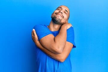 Hispanic adult man wearing casual blue t shirt hugging oneself happy and positive, smiling confident. self love and self care