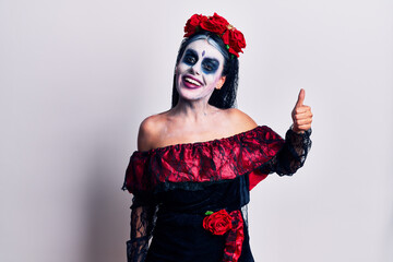 Young woman wearing mexican day of the dead makeup looking proud, smiling doing thumbs up gesture to the side