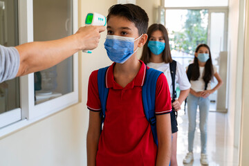 Teacher checking temperature of students with face mask for pandemic while children go back to school