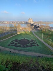 The Waalbrug arch bridge over the Waal River. Nijmegen city coat of arms made from plants in front. Nijmegen, Gelderland, Netherlands.