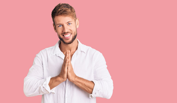 Young caucasian man wearing casual clothes praying with hands together asking for forgiveness smiling confident.