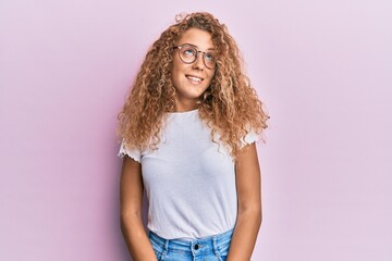 Beautiful caucasian teenager girl wearing white t-shirt over pink background looking away to side with smile on face, natural expression. laughing confident.