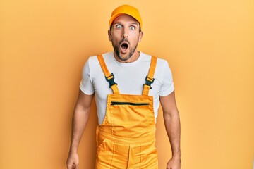 Young handsome man wearing handyman uniform over yellow background afraid and shocked with surprise...