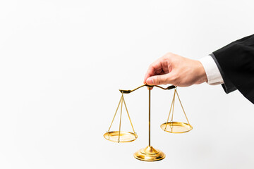 Judge or lawyer in with shirt, gray suit and robe is using his hand to hold golden justice's scales against the white background.