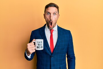 Handsome business man with beard drinking from i am the boss coffee cup scared and amazed with open mouth for surprise, disbelief face
