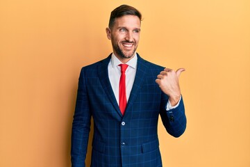 Handsome man with beard wearing business suit and tie smiling with happy face looking and pointing...