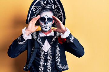 Young man wearing mexican day of the dead costume over yellow suffering from headache desperate and stressed because pain and migraine. hands on head.