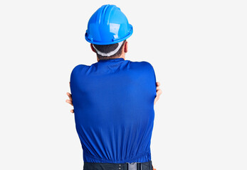 Young handsome man wearing worker uniform and hardhat posing backwards pointing ahead with finger hand