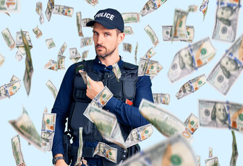 Young handsome man wearing police uniform pointing with hand finger to the side showing...