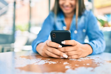 Young latin woman smiling happy using smartphone at coffee shop terrace.