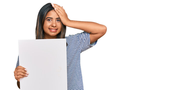 Young latin girl holding blank empty banner stressed and frustrated with hand on head, surprised and angry face