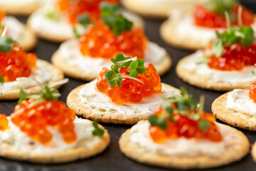 Salmon caviar and soft cheese savory crackers with sesame and poppy seeds served on black slate board