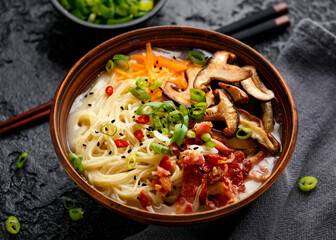 Pork bone Japanese style ramen noodle soup with crispy bacon, shiitake mushrooms and spring onions in clay bowl