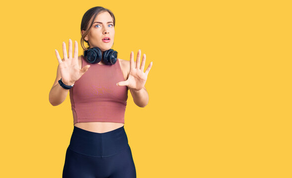 Beautiful caucasian young woman wearing gym clothes and using headphones doing stop gesture with hands palms, angry and frustration expression