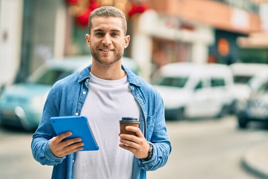 Young caucasian man smiling happy using touchpad and drinking coffee at the city.