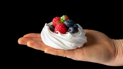 Woman's Hand hold meringue nest mini pavlova cake with fresh berries strawberry blueberry raspberry...