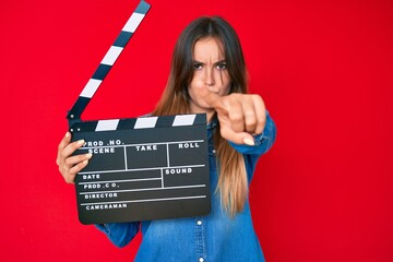 Beautiful caucasian woman holding video film clapboard pointing with finger to the camera and to...