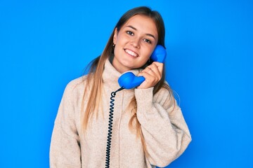 Beautiful caucasian woman speaking on vintage telephone looking positive and happy standing and...