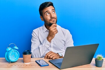 Handsome hispanic man working using laptop at the office thinking concentrated about doubt with...