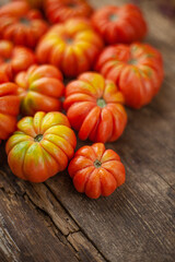 Red ribbed tomatoes on a wooden background. American or Florentine variety Nina. Food on the table top view. Autumn harvest of vegetables similar to flowers and pumpkins.Ribby tomato.