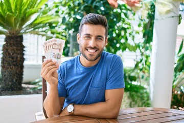 Young hispanic man smiling happy holding chinese yuan banknotes at the terrace.