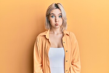 Young blonde girl wearing casual clothes puffing cheeks with funny face. mouth inflated with air,...
