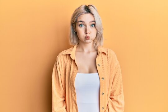 Young blonde girl wearing casual clothes puffing cheeks with funny face. mouth inflated with air, crazy expression.