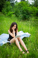 Outdoor picnic. A girl reads a book in the open air while sitting on a blue plaid. The girl enjoys the fresh air. Outdoor recreation, close-up.