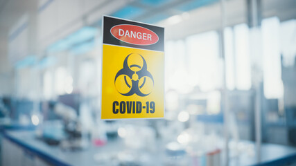 Danger Covid-19 Sign on the Glass Door of Virology and Medical Research Laboratory: Team of Scientists Wearing Masks and Coveralls Work on Covid-19 Cure, Vaccine, Developing Antibiotics, Drugs