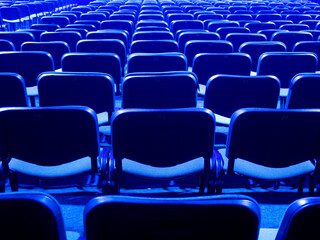 Blue chairs are placed on a row in an auditorium