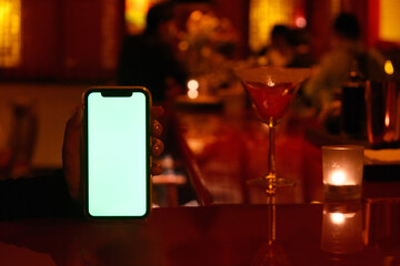 close up one hand showing green screen phone at night bar 