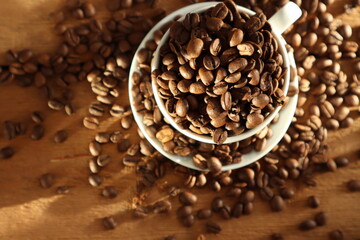 Coffee beans in a white cup on a wooden surface in the sun.