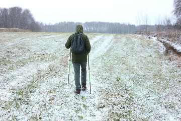 A man with a green winter jacket trains in the field. Nordic walking.