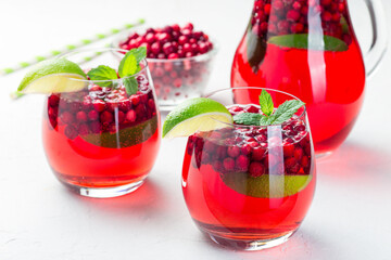 Lingonberry and lime punch or limeade in glass and pitcher on gray background, horizontal