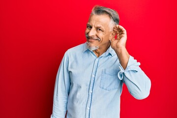Middle age grey-haired man wearing casual clothes smiling with hand over ear listening an hearing to rumor or gossip. deafness concept.