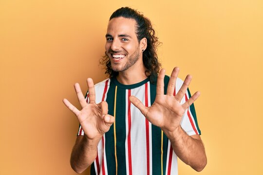 Young handsome man with long hair wearing casual clothes showing and pointing up with fingers number eight while smiling confident and happy.