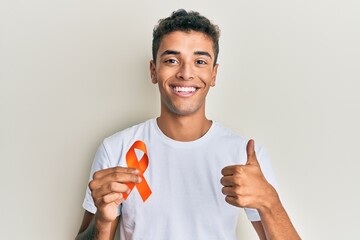 Young handsome african american man holding awareness orange ribbon smiling happy and positive,...