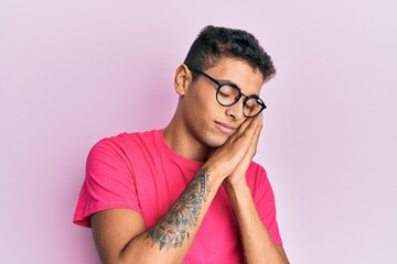 Young handsome african american man wearing glasses over pink background sleeping tired dreaming...