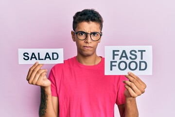 Young handsome african american man holding salad and fast food message paper skeptic and nervous, frowning upset because of problem. negative person.