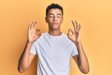 Young handsome african american man wearing casual white tshirt relax and smiling with eyes closed doing meditation gesture with fingers. yoga concept.