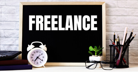 The word FREELANCE is written on the chalkboard next to the white alarm clock, glasses, potted plant, and pencils in a stand