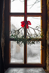 Branch of christmas mistletoe with red bow on window background