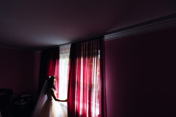 bride in wedding dress and bridal veil opened the curtains in th