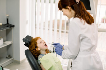Beautiful smile with white teeth. A dentist examines the oral cavity of a young beautiful girl through a magnifying glass in the dental office.