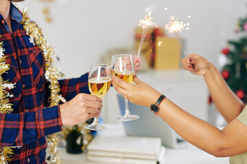 Hands of coworkers burning Bengal lights and toasting with champagne glasses when celebrating New Year in office