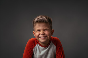 Funny small boy happily smiling on camera isolated on dark gray or black background. Portrait of young boy portrait on black. Emotional little boy on gray background. 